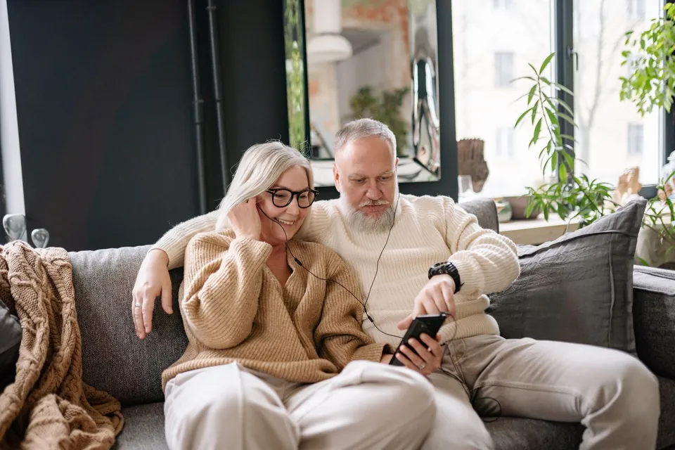 An older couple sitting on a couch at home, listening to music together